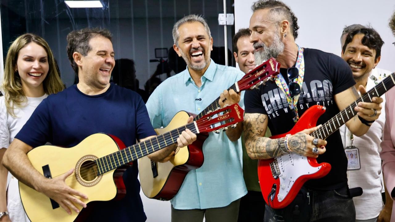 O prefeito Evandro Leitão e o Governador Elmano de Freitas fingem tocar violões, ao lado deles há um músico com uma guitarra na mão, e outros gestores e representantes da Prefeitura também aparecem na foto